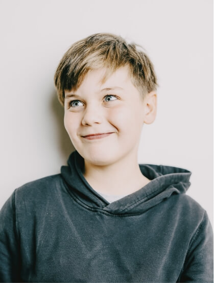 Ein Junge in grauem Hoodie lächelt verschmitzt