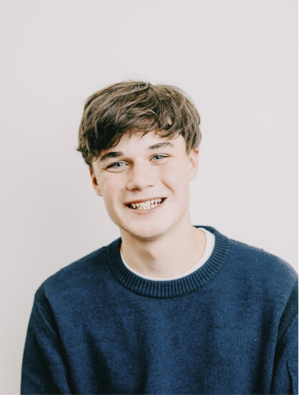 Ein Teenager in blauem Strickpulli lächelt strahlend in die Kamera